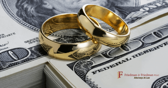Two golden wedding bands sit on top of a 100-dollar bill