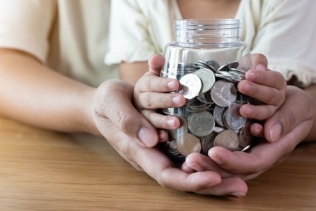 Hands of Parent and Child with Jar of Coins